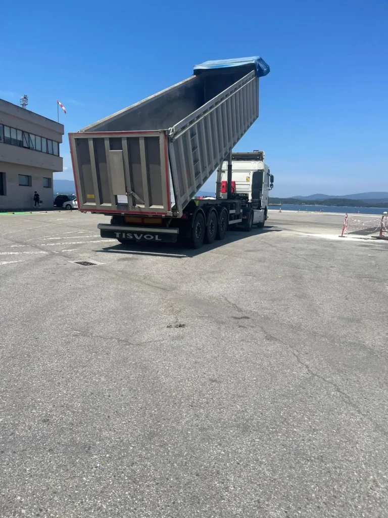 Camión de Transportes Jamardo descargando con la bañera elevada junto a una nave industrial